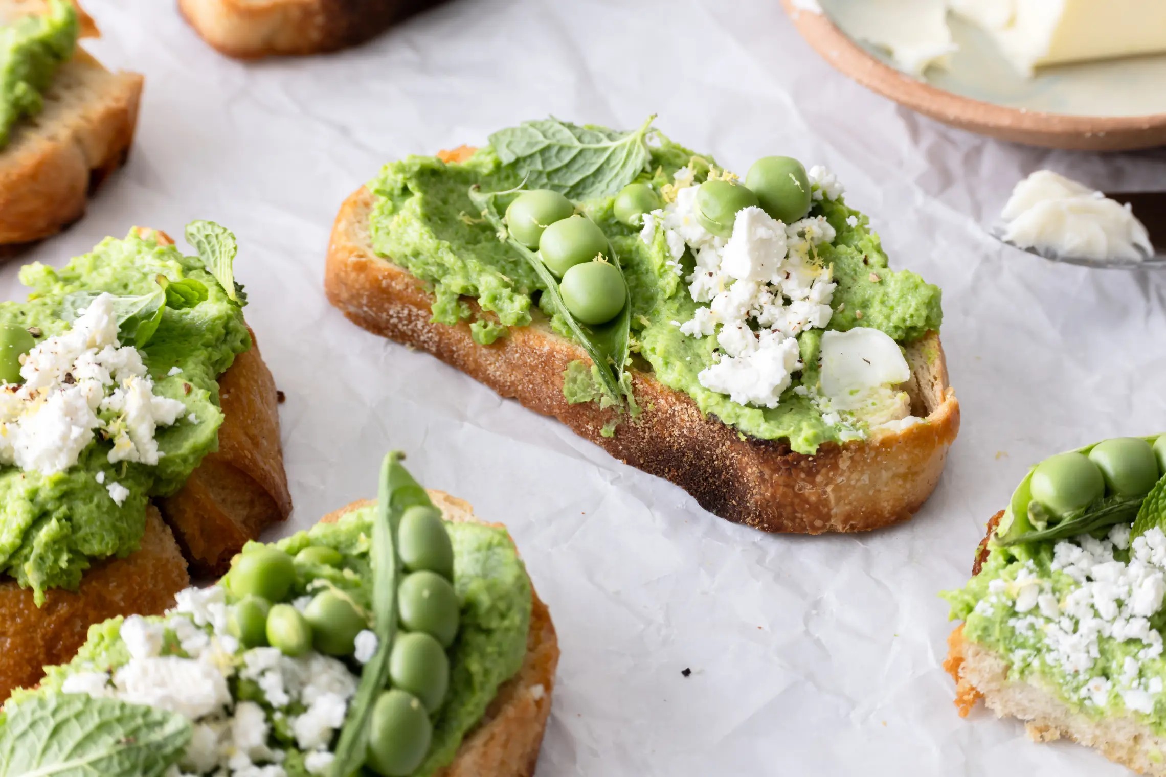 Platter of vibrant spring pea and mint crostini, garnished with edible flowers and lemon zest