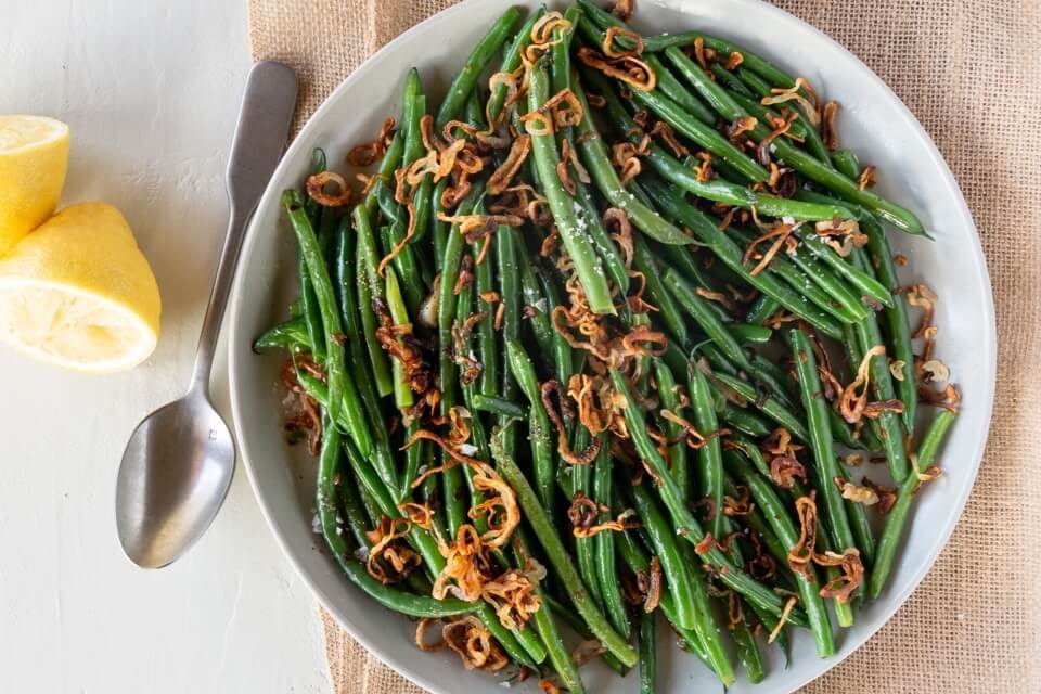 close up plate of butter braised green beans with golden brown shallots