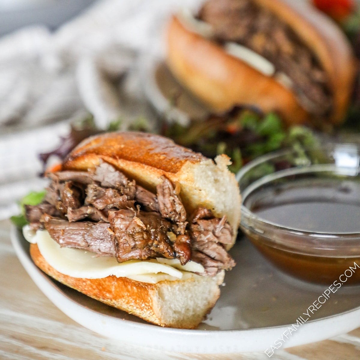 close-up of crockpot french dip sandwiches with a rich, dark au jus dipping bowl