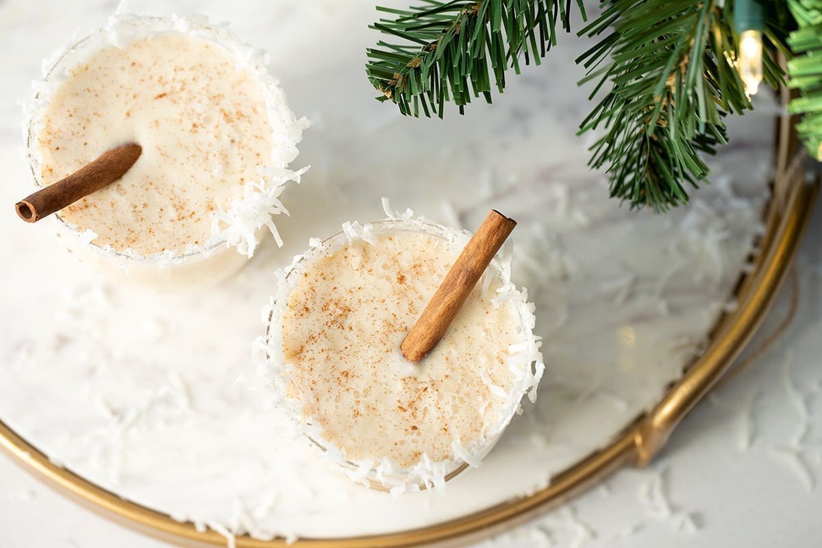 Creamy velvet coquito in ornate glasses with cinnamon sticks and nutmeg, festive holiday setting