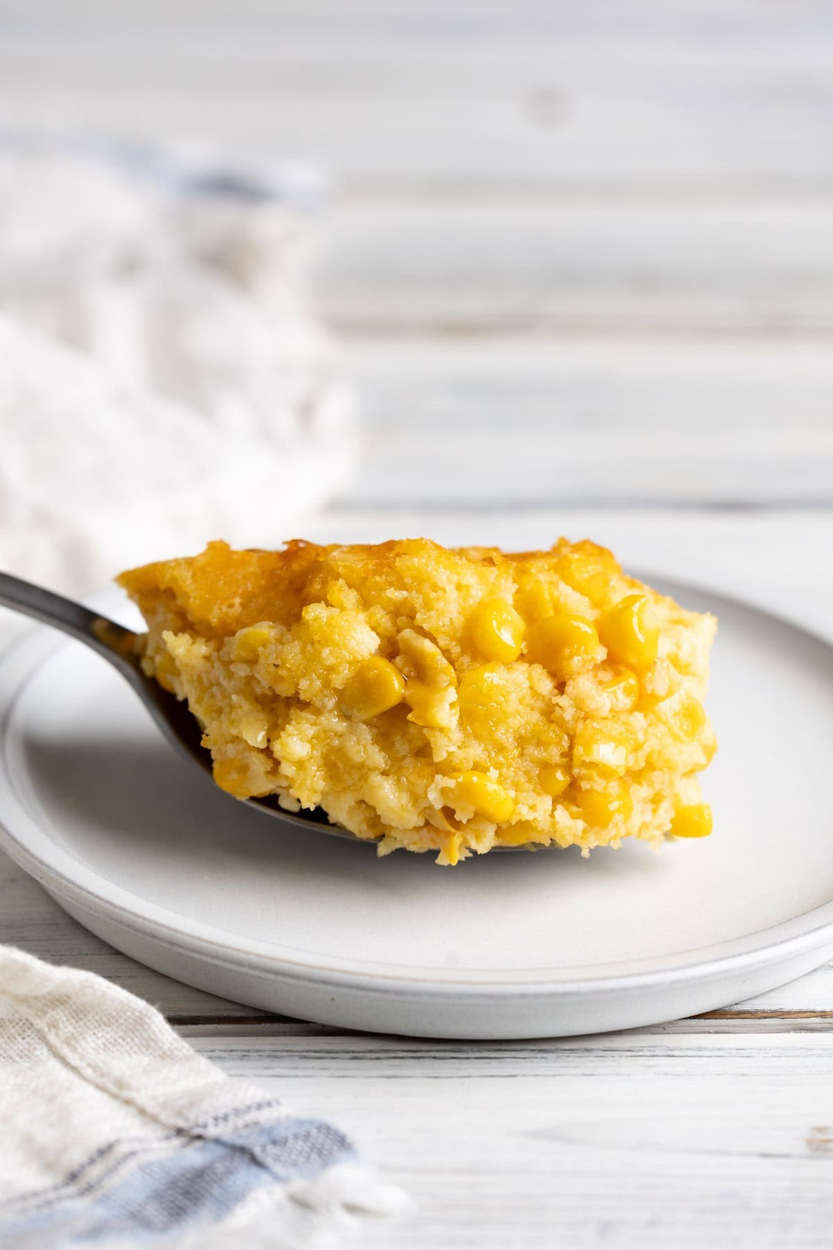 golden brown corn casserole with a visible melted butter center, rustic table setting, warm lighting