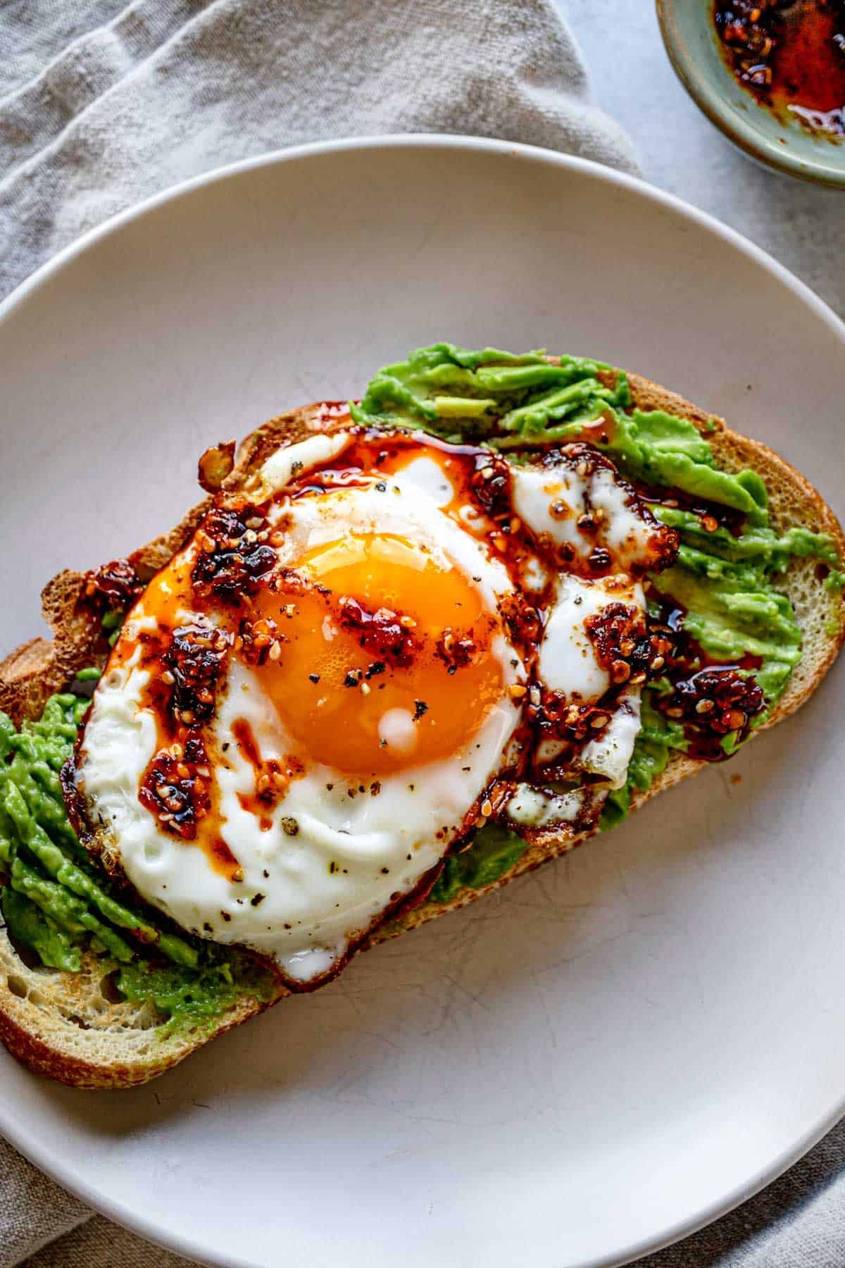 Perfectly plated avocado egg toast with runny yolk and chili flakes, bright natural light