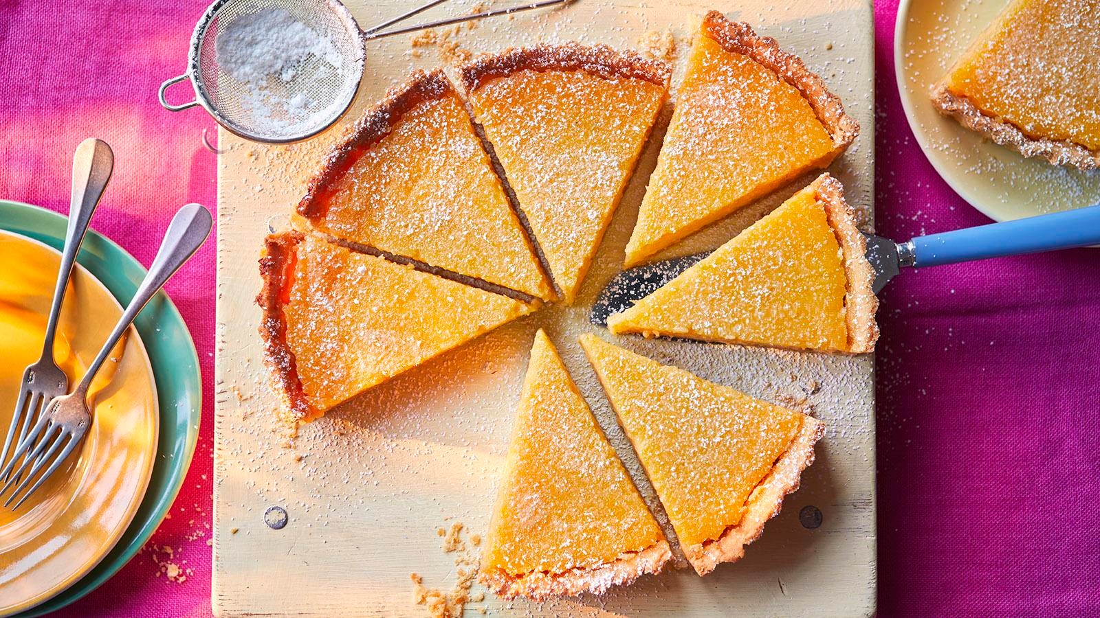 Close-up of a festive lemon tart with a golden, flaky crust, garnished with sugared cranberries and rosemary sprigs, holiday setting