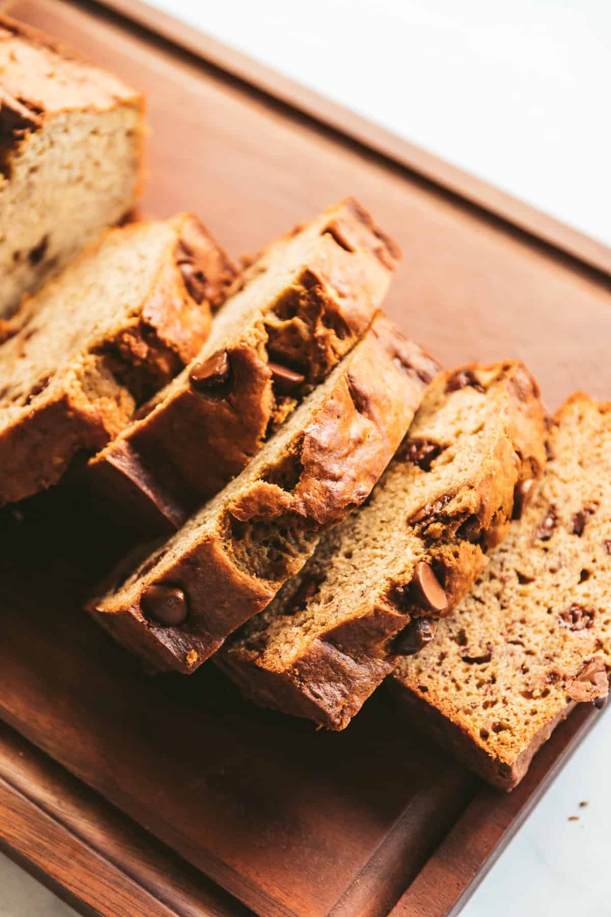Warm slice of browned butter banana bread on a rustic wooden board with a cup of coffee, cozy kitchen background
