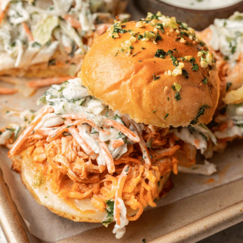 A vibrant platter of buffalo chicken sliders, topped with a sprinkle of green onions and a side of creamy blue cheese dip, ready for a party.
