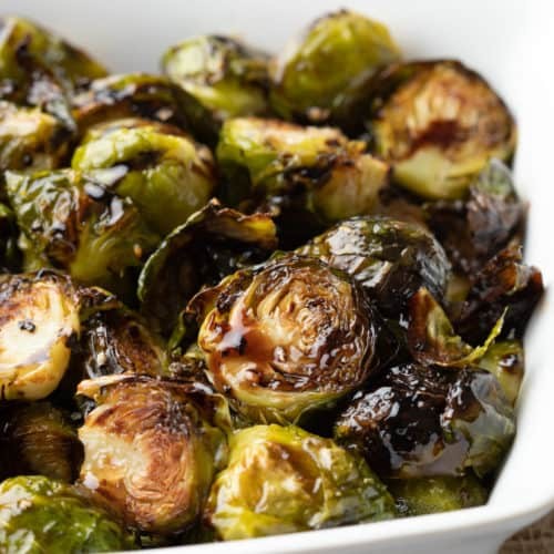 Vibrant close-up of perfectly roasted Brussels sprouts with a glossy balsamic glaze, garnished with fresh herbs, in a rustic serving dish.