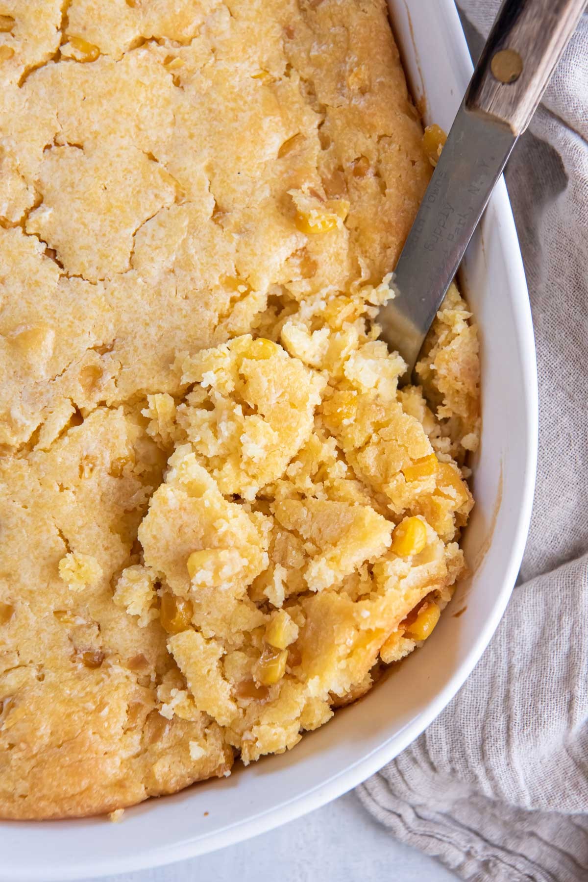 Golden brown sweet corn casserole in a rustic baking dish, close up with steam.