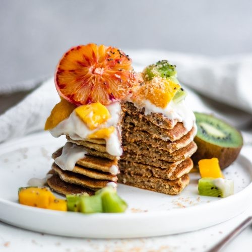 stack of kiwi coconut pancakes topped with fresh fruit and coconut flakes