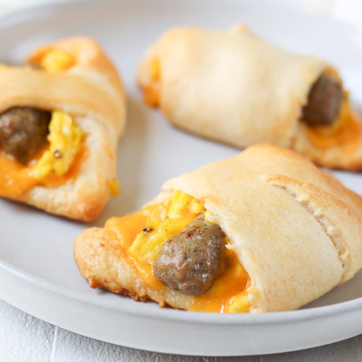 Golden crescent pastry roll-ups filled with sausage and scrambled egg, on a baking sheet, warm morning light, close-up
