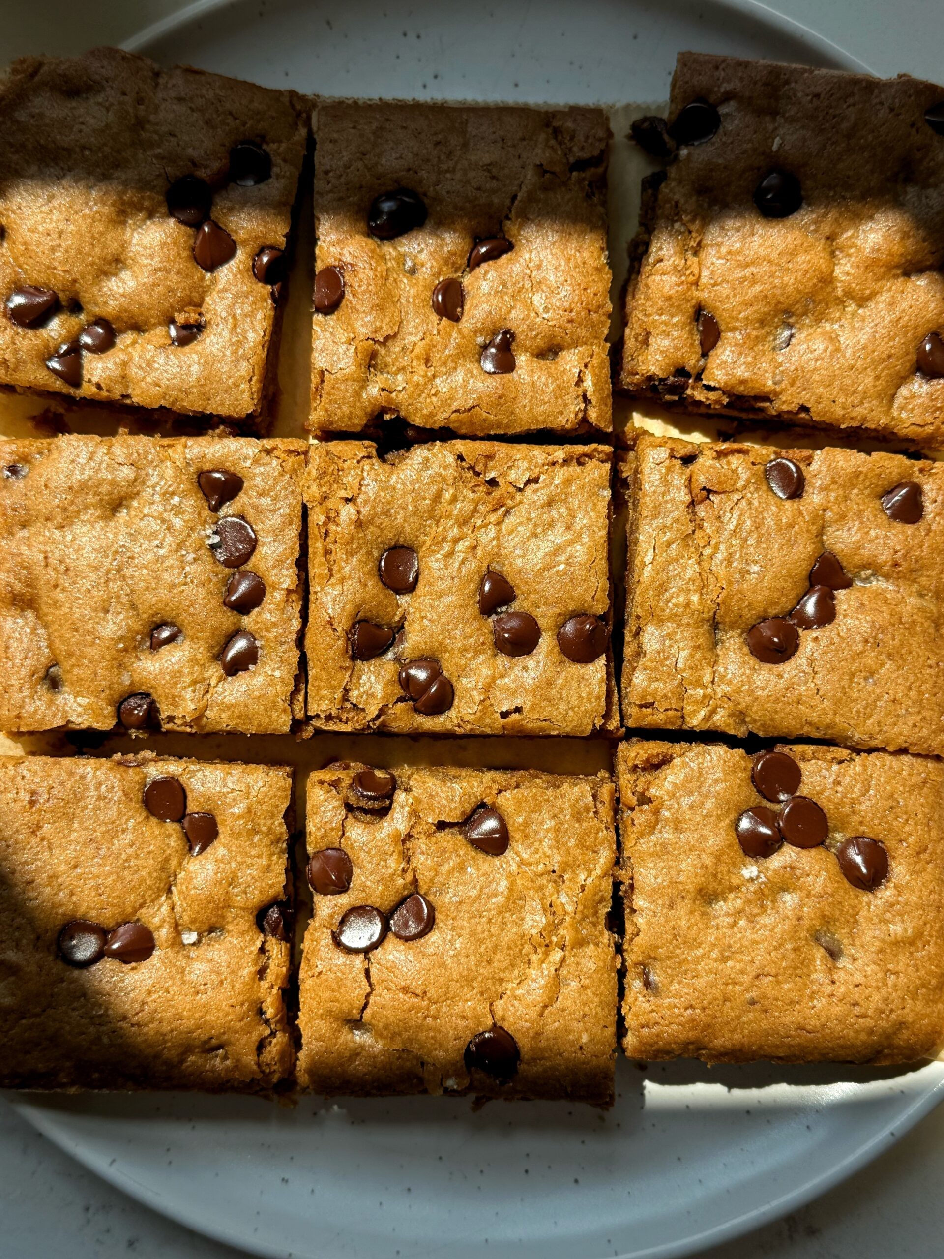 freshly baked choco-chunk cookie bars on a cooling rack, cut into squares, with some melting chocolate chips