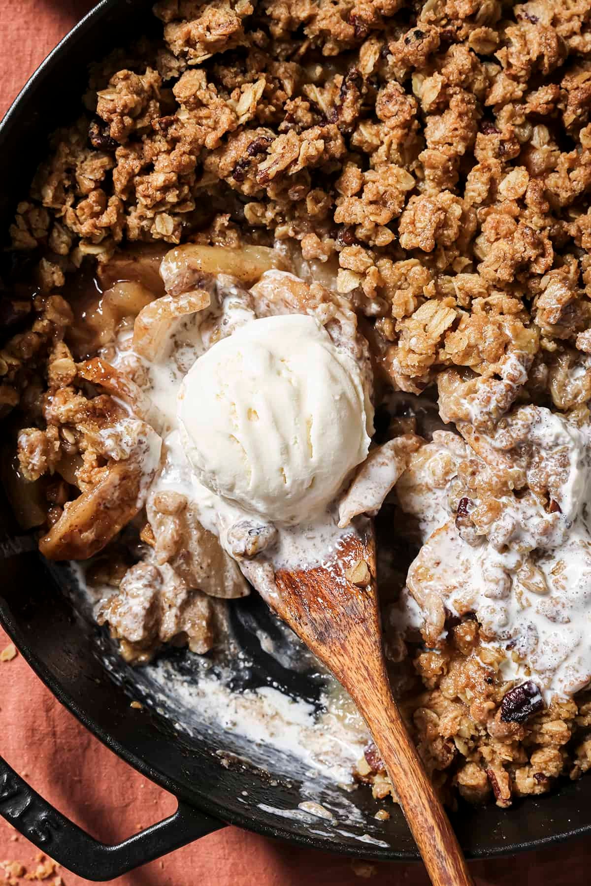 overhead shot of a rustic apple crisp with a scoop of vanilla ice cream, served in a cast iron skillet