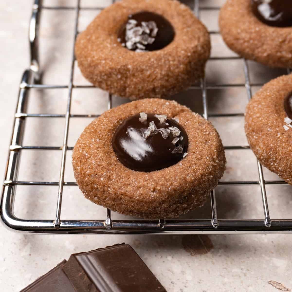 Close-up of freshly baked chocolate thumbprint cookies with shiny chocolate ganache filling, on a cooling rack