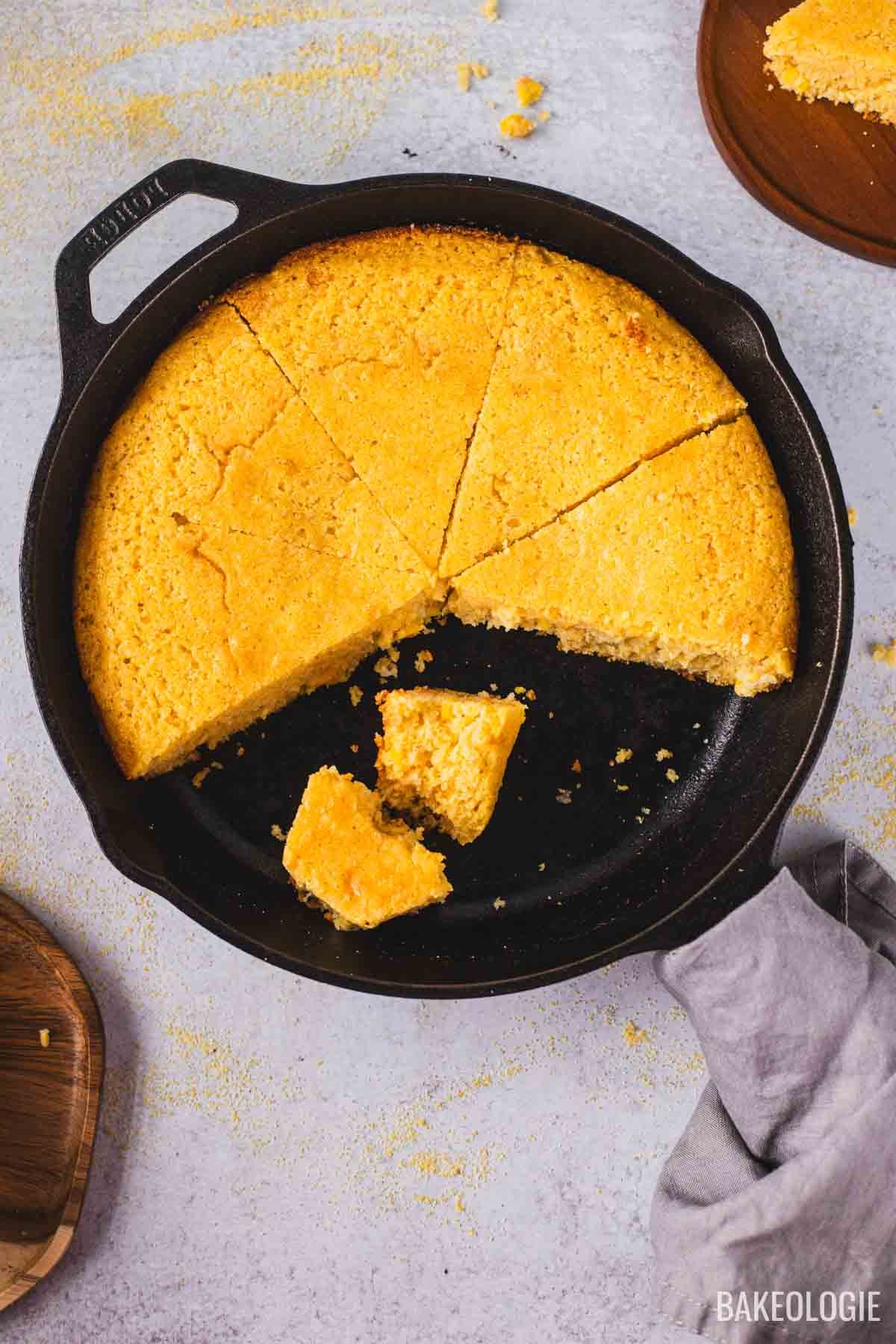 Golden brown skillet cornbread cooling on a wire rack, steam gently rising, with a slice cut out to show tender, moist crumb.