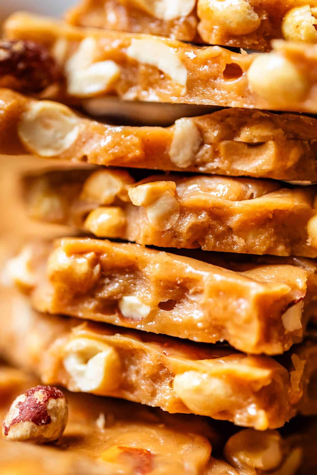 glossy, golden peanut brittle shards with whole peanuts scattered, on a rustic wooden board, natural light, close up