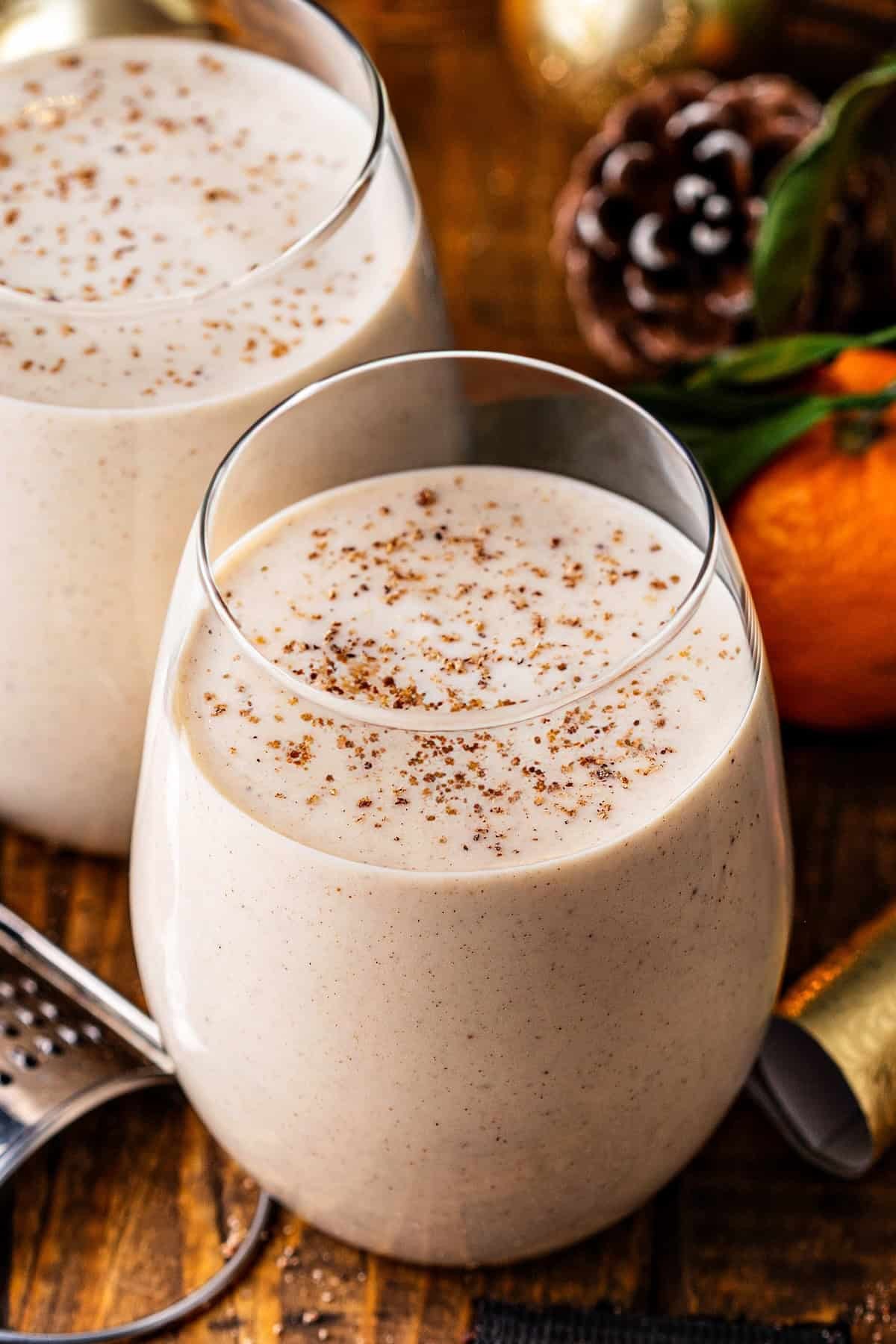 Traditional Puerto Rican Coquito drink garnished with cinnamon sticks and grated nutmeg, chilled in a glass