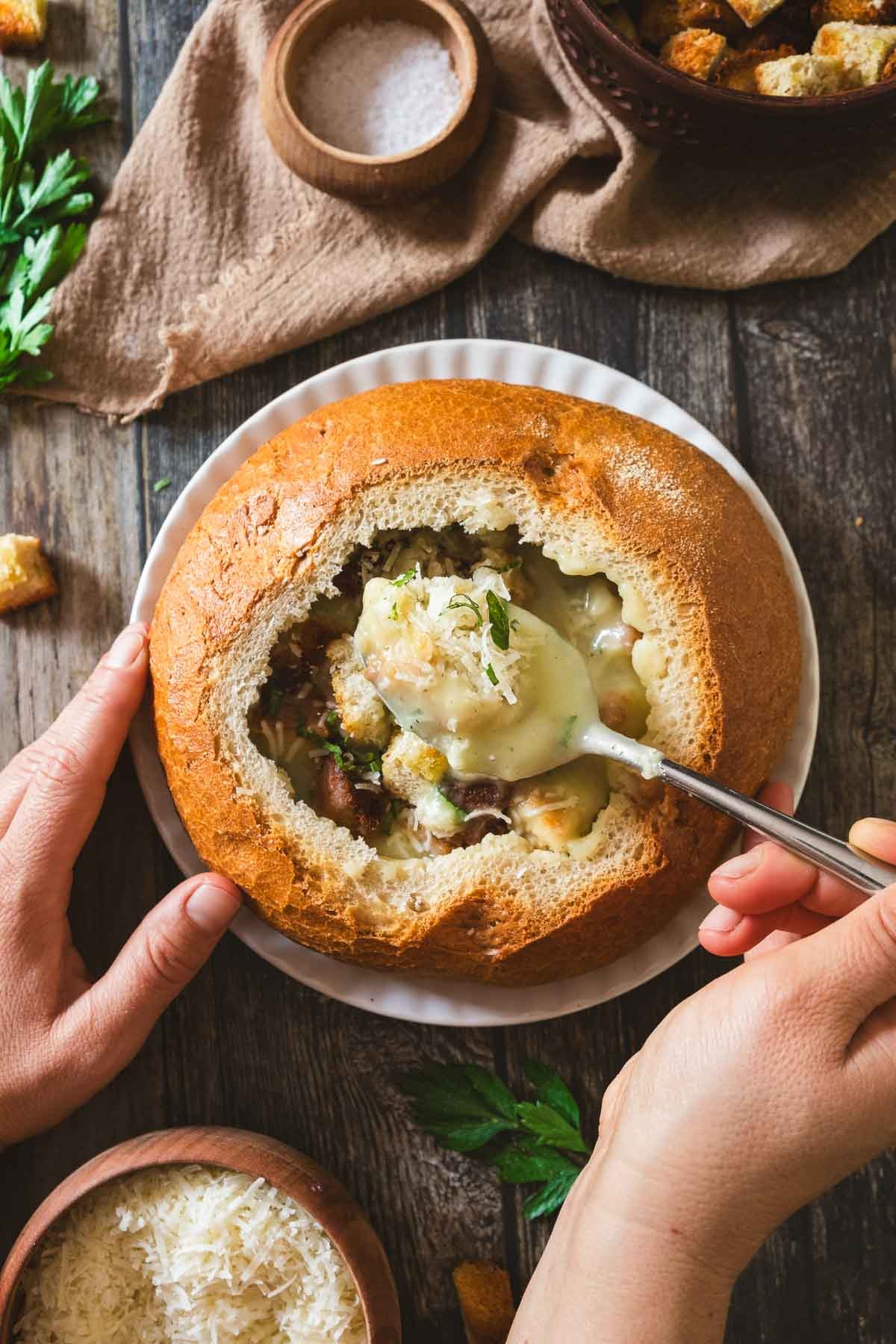 Cozy, steaming bowl of whipped garlic soup with crusty bread, garnished with fresh herbs