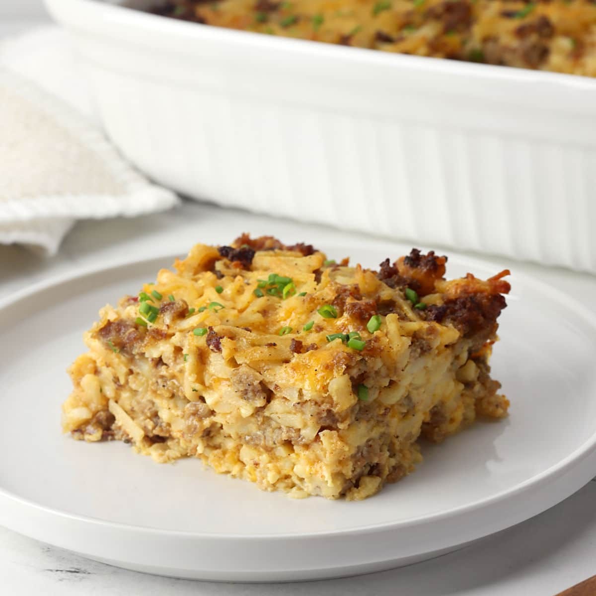 hearty breakfast casserole with golden hash browns, fluffy eggs, melted cheese, and crumbled sausage, served on a rustic wooden table with fresh chives garnish