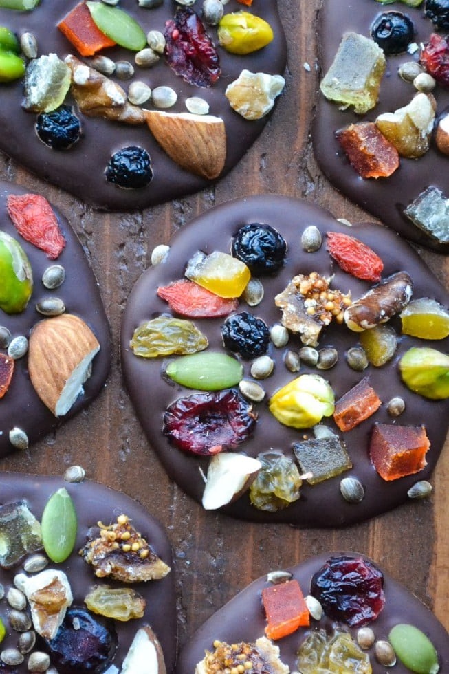 colorful dark chocolate mendiants with various dried fruits and nuts on parchment paper