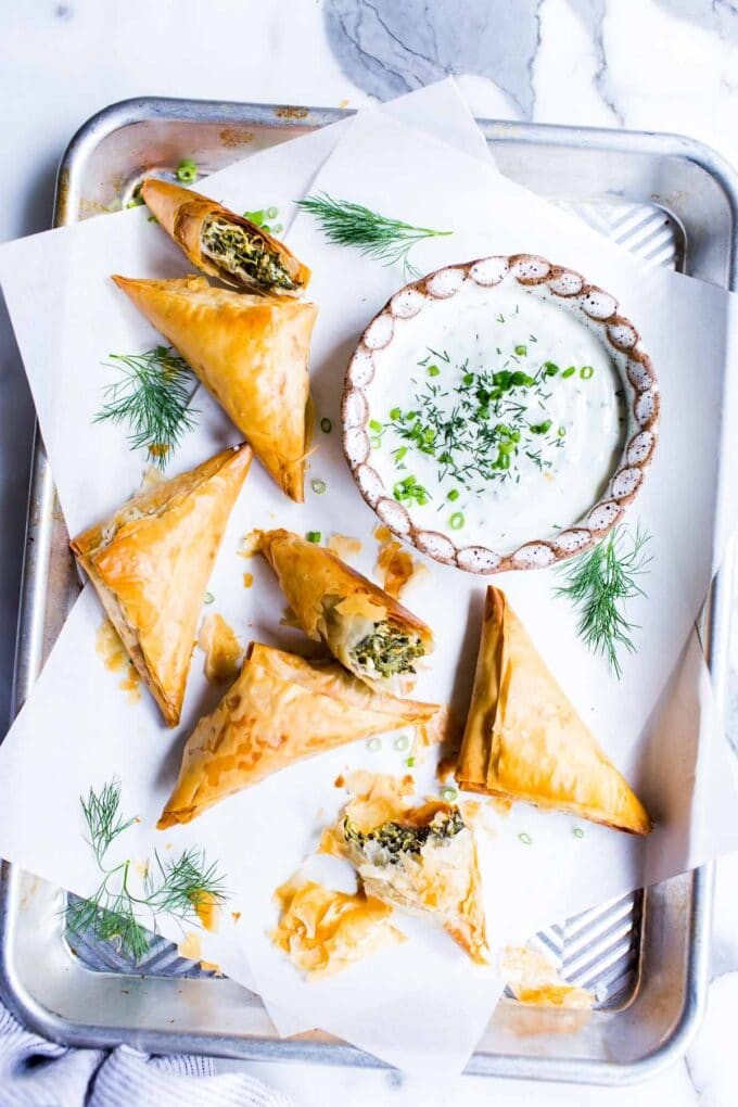 golden brown spinach feta pastry triangles on a white serving platter, garnished with fresh dill