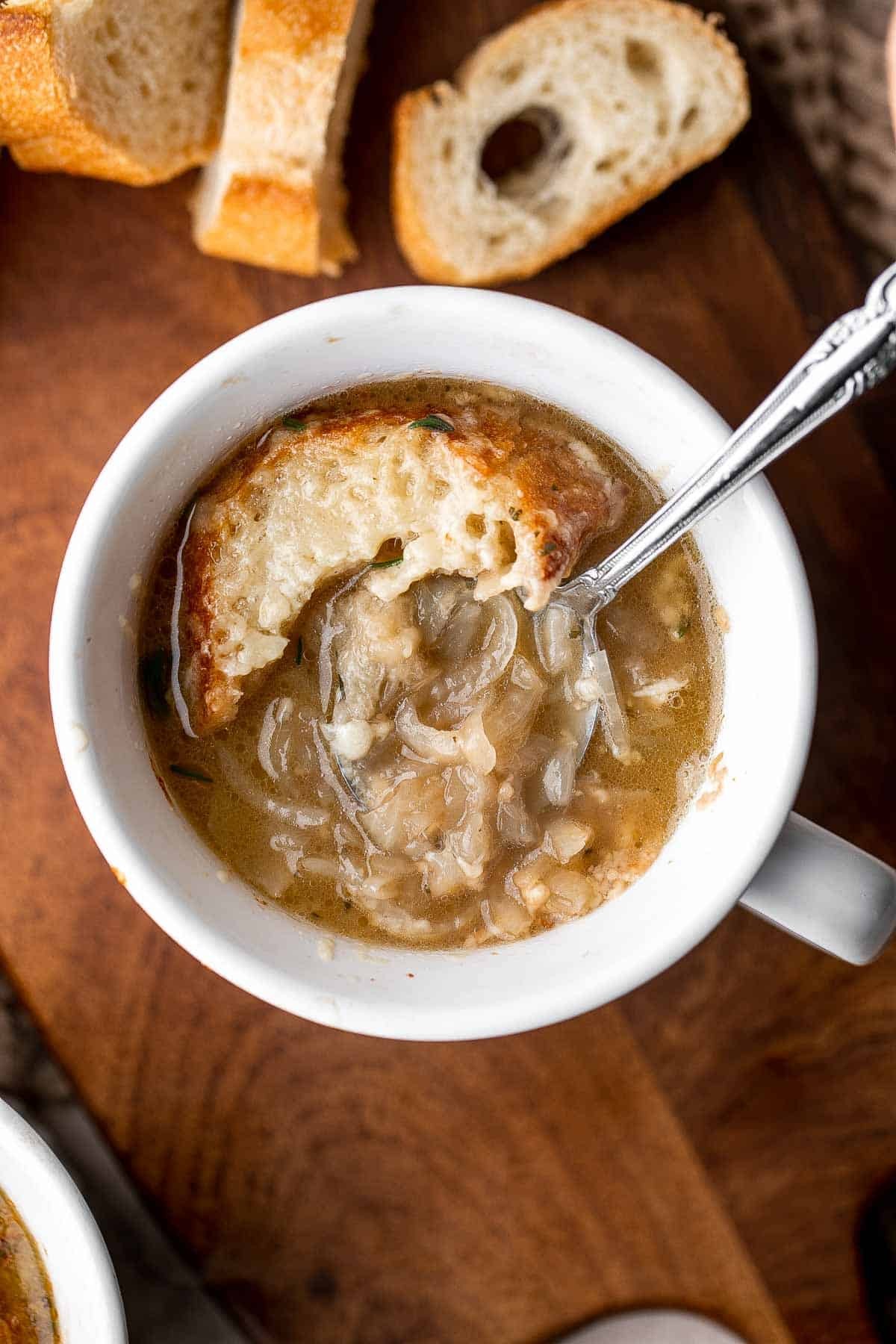A warm, inviting bowl of caramelized onion soup topped with toasted bread and melted cheese, with a rustic kitchen background and soft lighting
