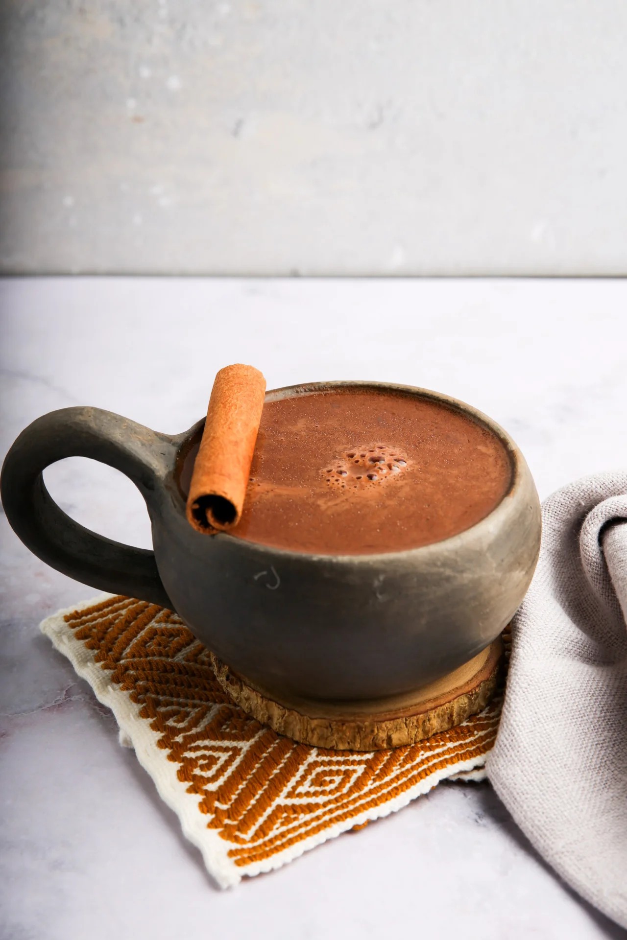 Rustic mug of Mexican spiced hot chocolate with cinnamon stick and chili, steam rising.