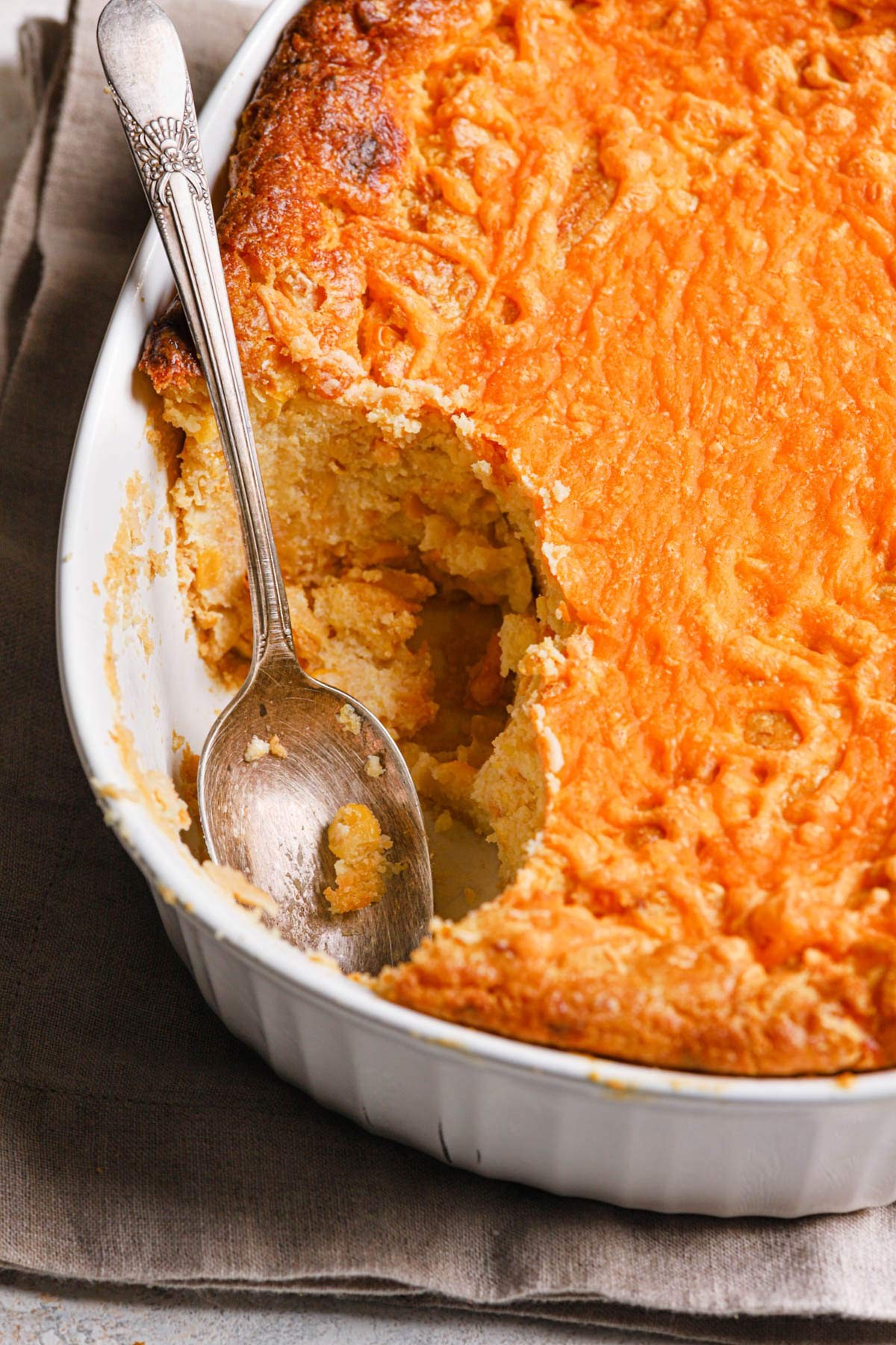 Golden brown creamy corn casserole with a spoon taking a scoop, family style, warm lighting