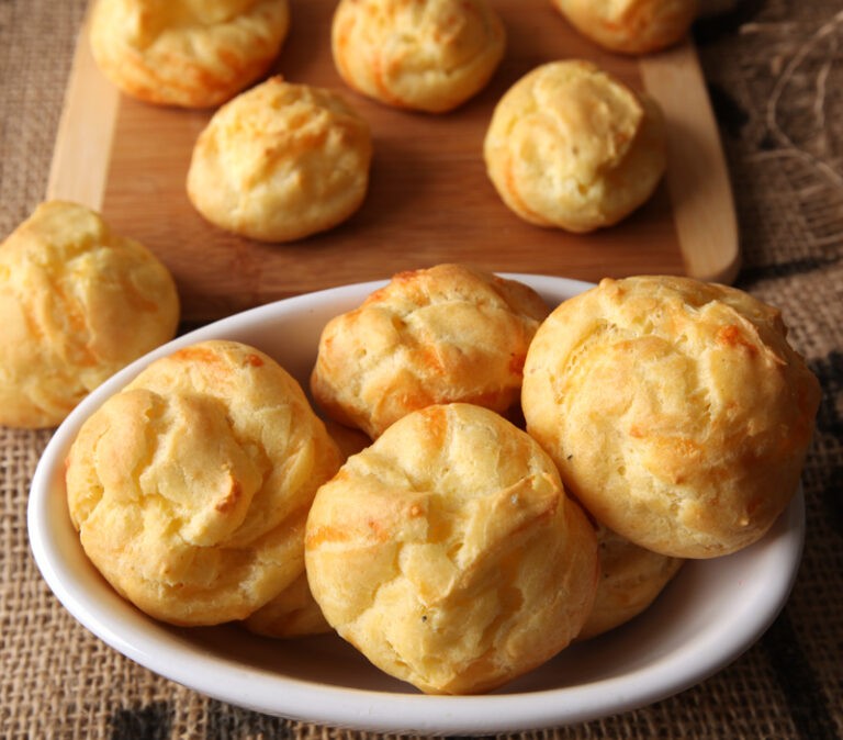 Golden brown savory cheese puffs on a parchment-lined baking sheet, steam gently rising, close-up with soft focus