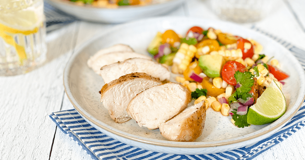 Vibrant healthy avocado dinner bowl with grilled chicken, cherry tomatoes, corn, and lime dressing on a light background