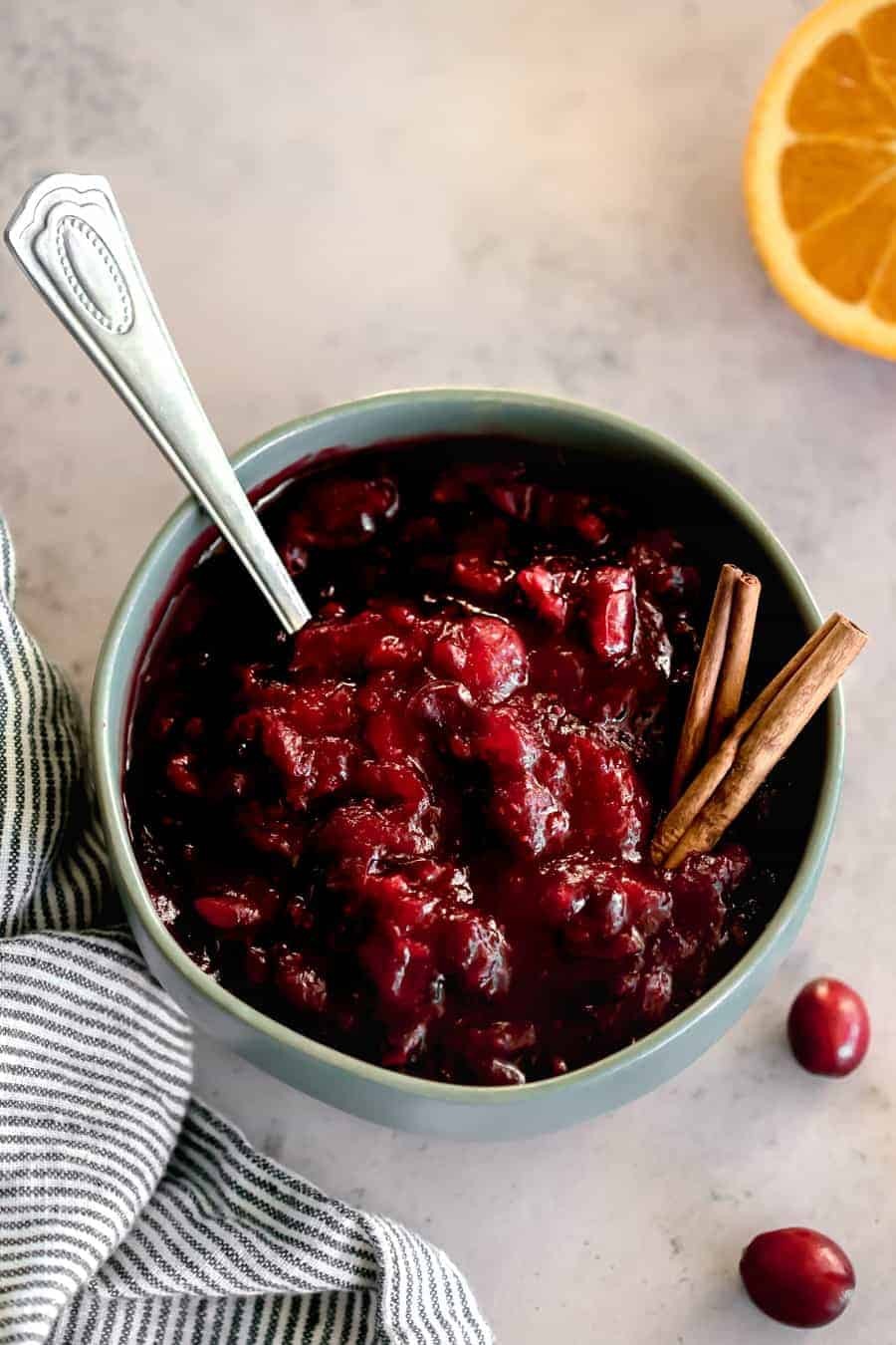 Homemade cranberry sauce with honey drizzle in a ceramic bowl, garnished with fresh cranberries and orange zest, on a rustic wooden table, holiday setting