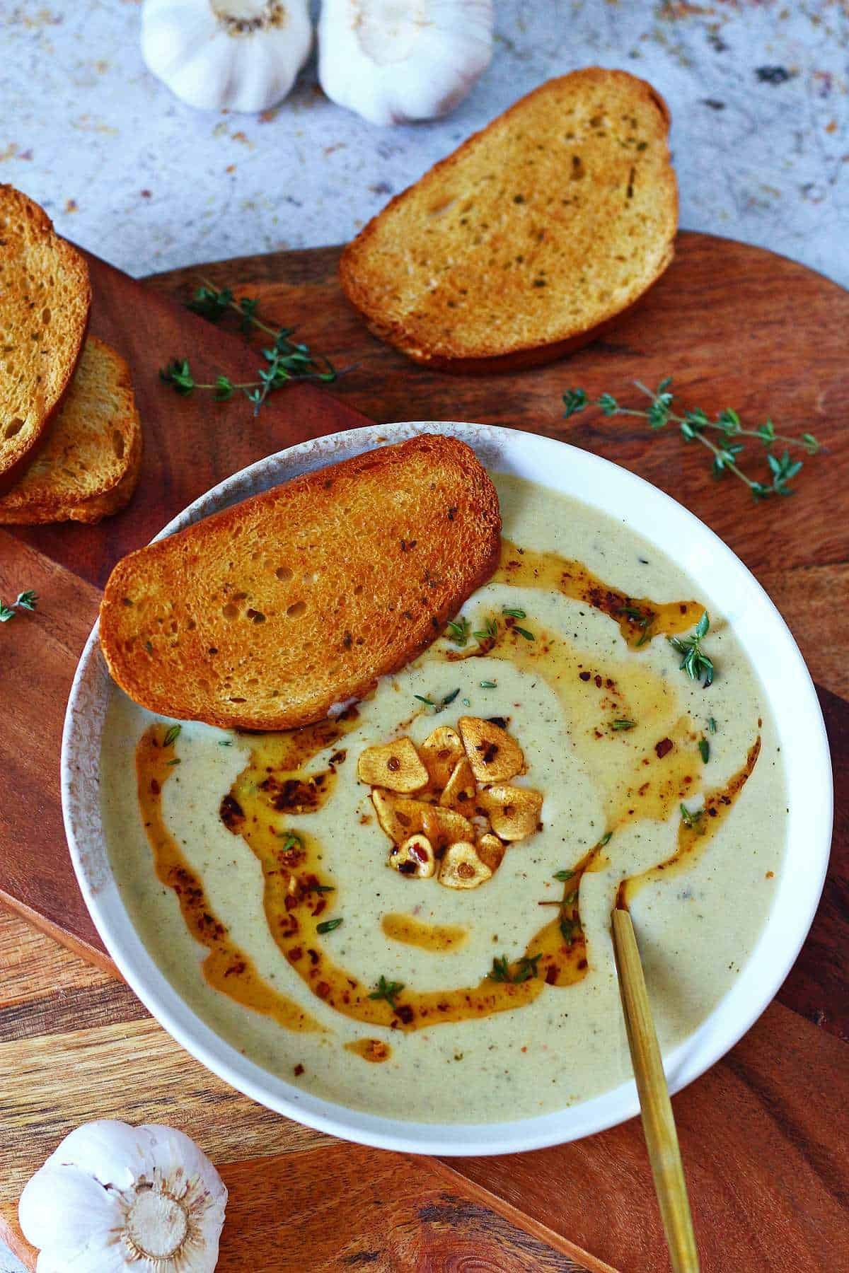 Steaming creamy roasted garlic and herb soup in a rustic bowl with crusty bread on a wooden table, cozy lighting