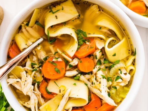 Steaming chicken noodle soup bowl with autumn leaves background, cozy kitchen setting, natural light