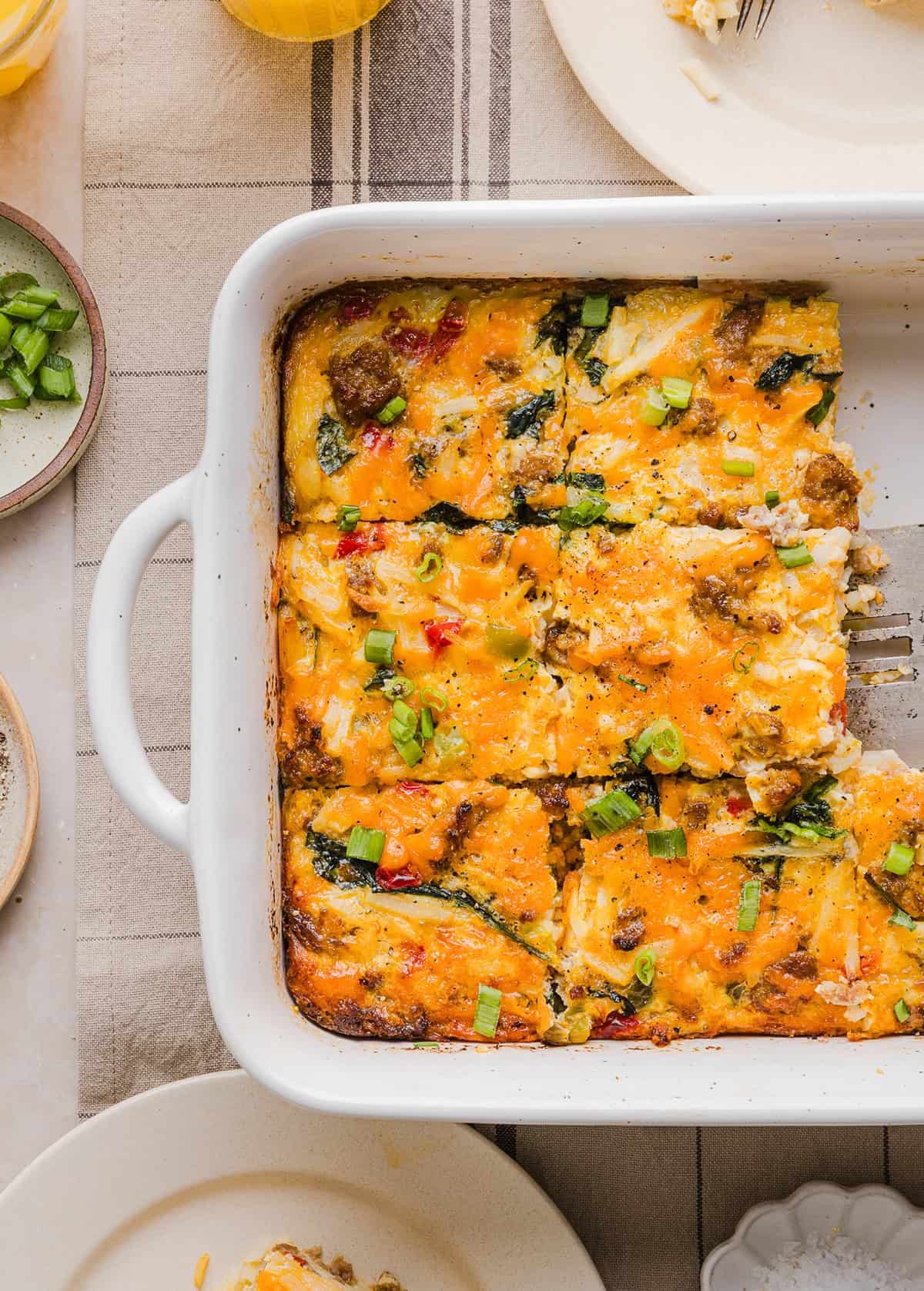 Delicious golden brown hash brown and egg breakfast casserole with melty cheese, garnished with fresh chives, served on a rustic wooden table.