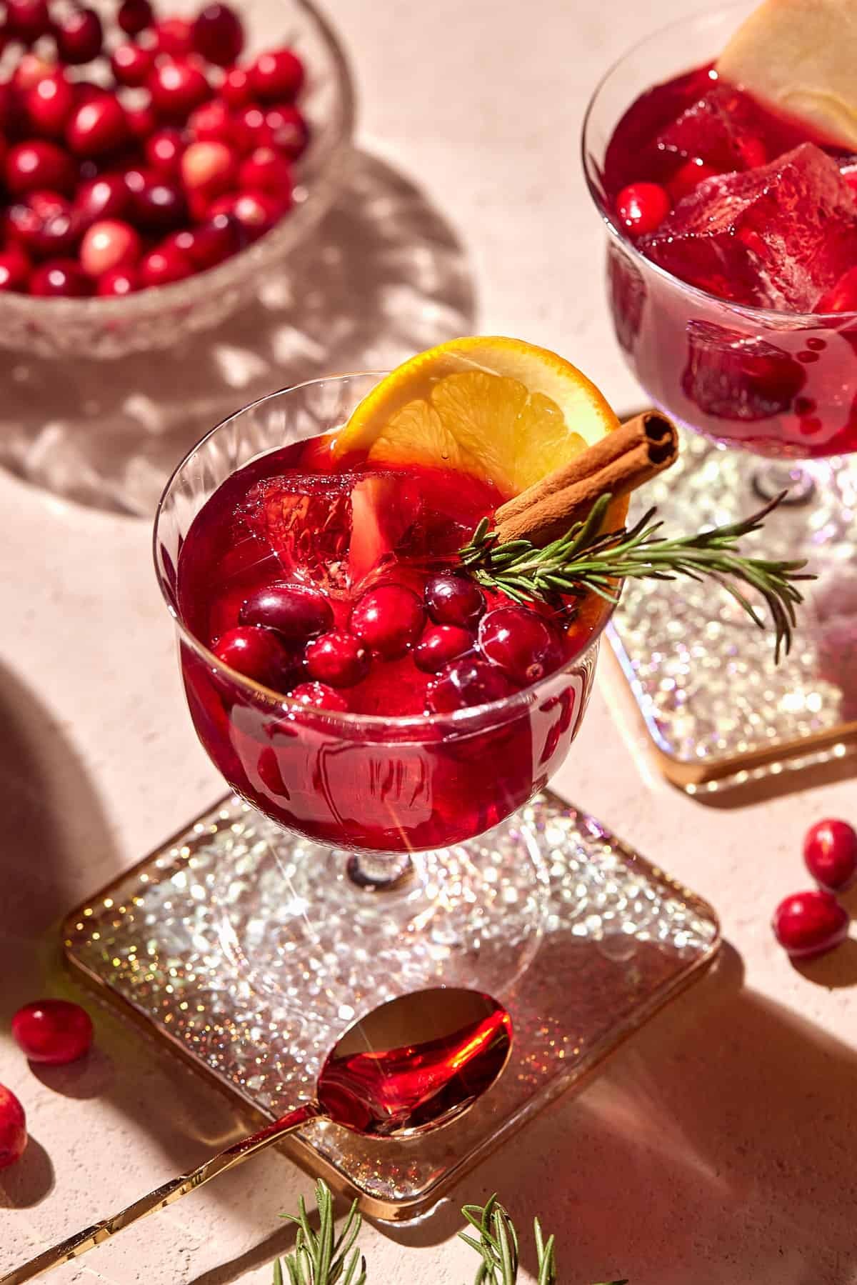 ruby red sangria in a crystal pitcher with cranberries, orange slices, and rosemary sprigs, holiday setting