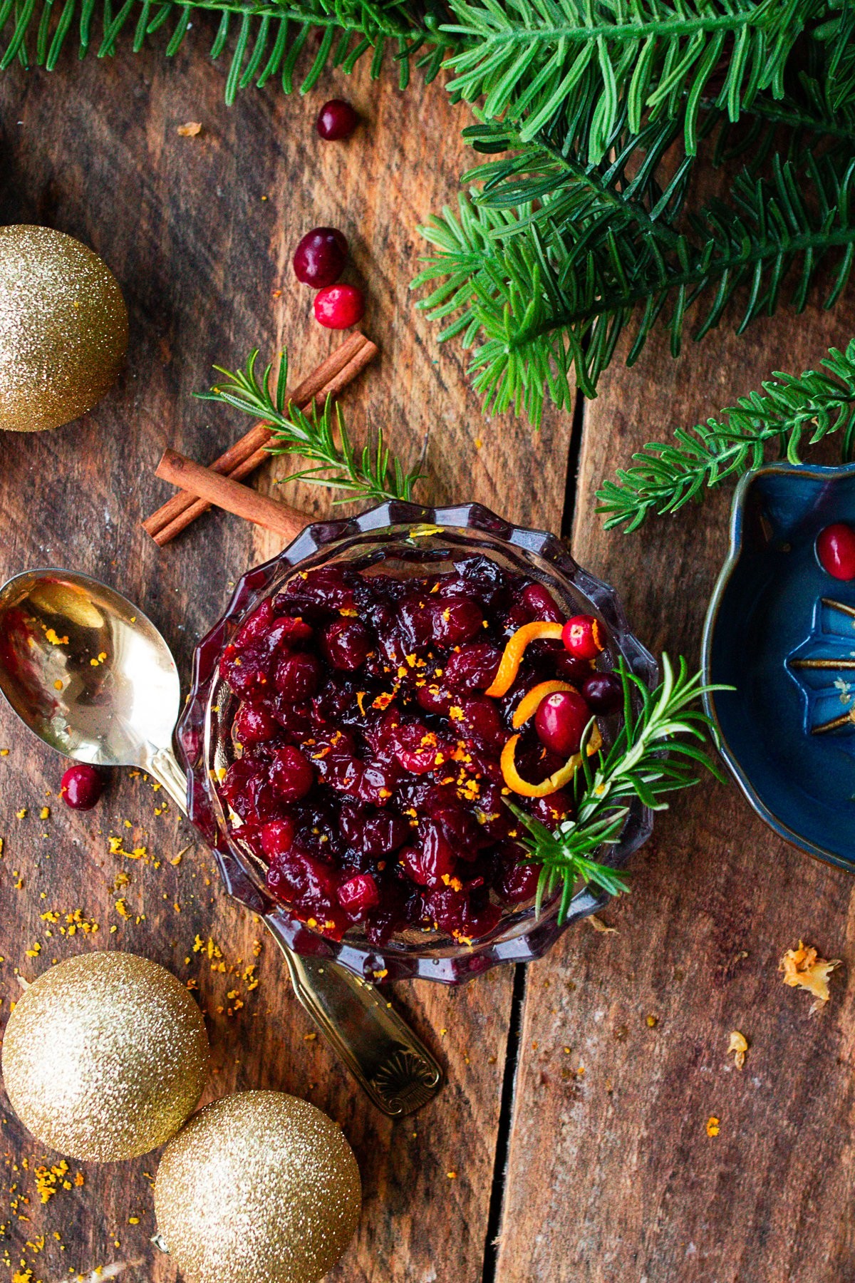 Homemade cranberry orange zest sauce in a beautiful serving bowl, garnished with fresh cranberries and orange slices, on a rustic wooden table with holiday decor