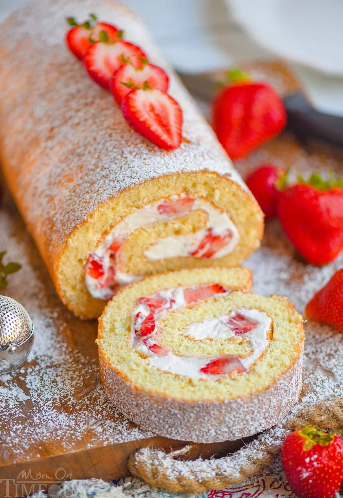 Pillowy Strawberry Shortcake Roll on a rustic wooden board, garnished with fresh strawberries and mint, soft natural light