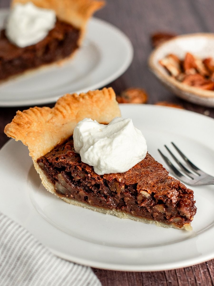 Close-up of a rich, fudgy chocolate pecan pie slice with a scoop of vanilla ice cream