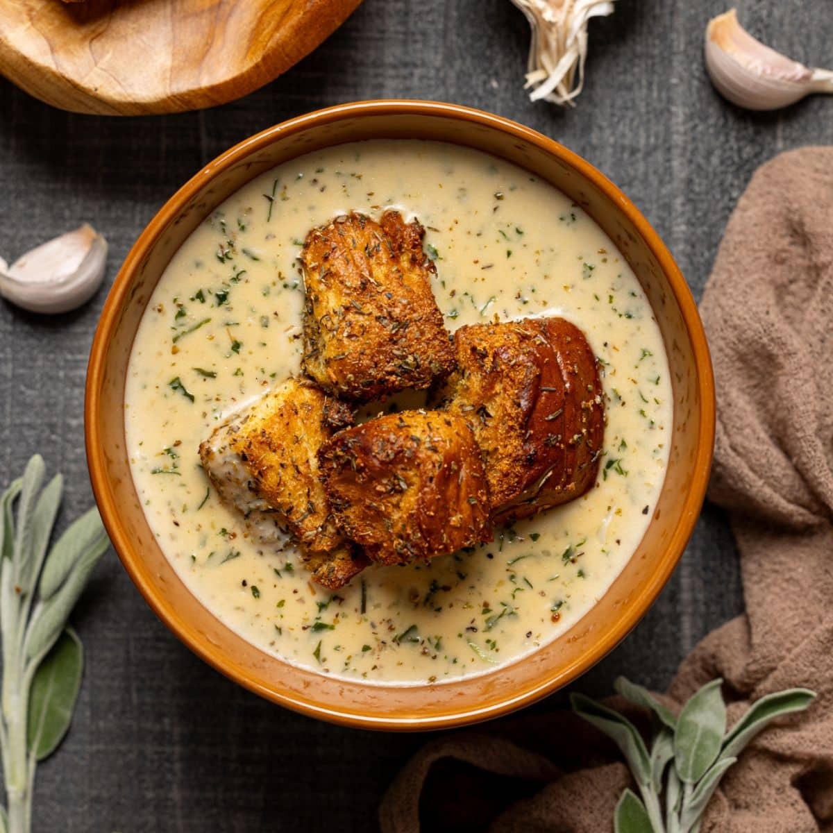 Hearty bowl of creamy Parmesan garlic soup with fresh herbs and a crusty bread slice on a rustic wooden table