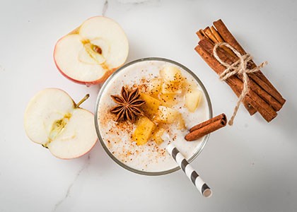 a vibrant spiced apple protein smoothie in a glass with apple slices and cinnamon sticks as garnish