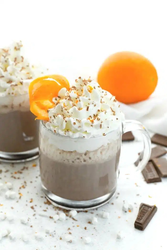 Gourmet orange infused hot chocolate with whipped cream and orange zest, cozy winter setting