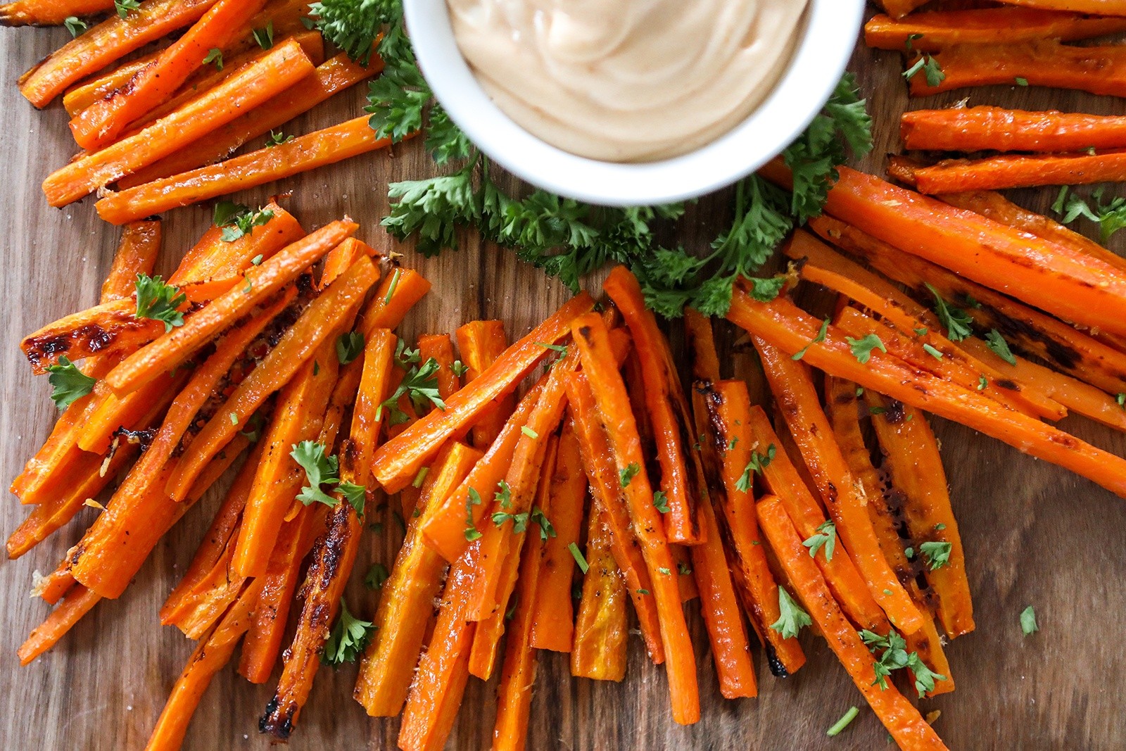 close up of apple cider vinegar glazed carrot fries on a rustic wooden board