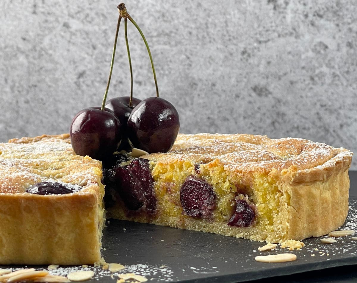 close up of a slice of cherry plum and almond tart with a glass of cherry liqueur