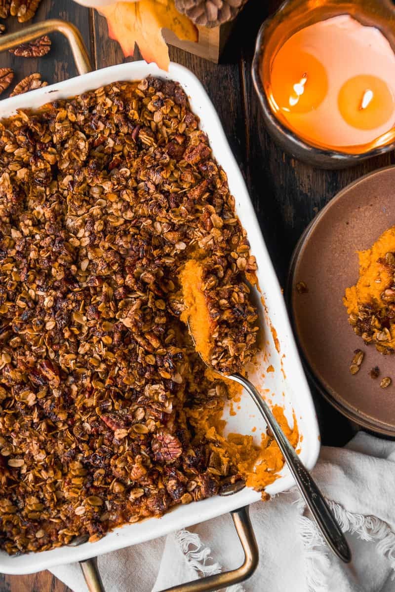 Rustic maple sweet potato casserole with pecan crunch topping, golden brown and steaming, on a wooden table with fall decor