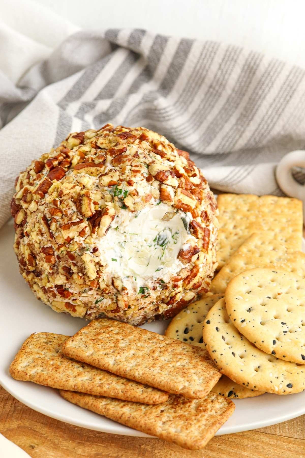 Herbed cheese ball with mixed nut crust on a serving platter with crackers, rustic background