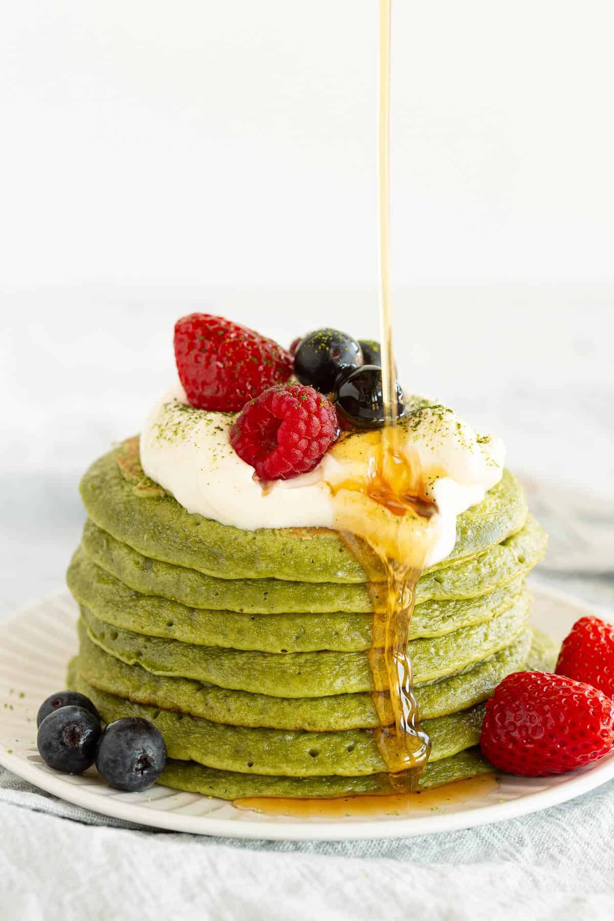 stack of matcha green tea pancakes with berries and syrup
