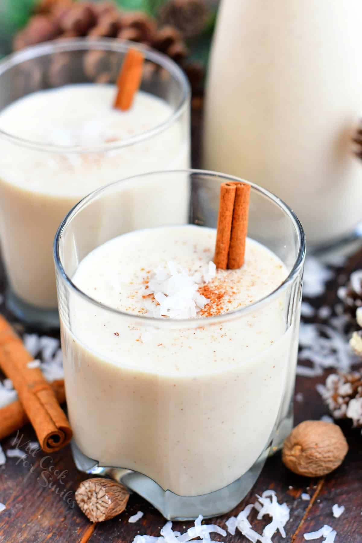 beautifully styled coquito drink in a glass with cinnamon stick and grated nutmeg, festive holiday background