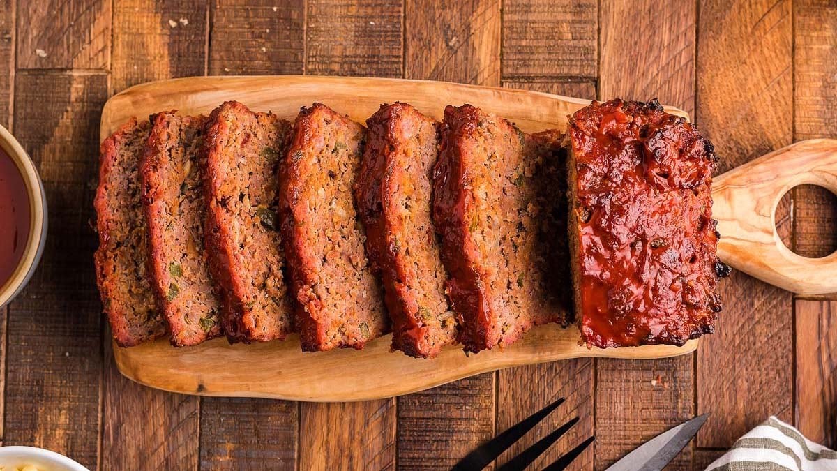 homemade meatloaf being sliced on a wooden cutting board