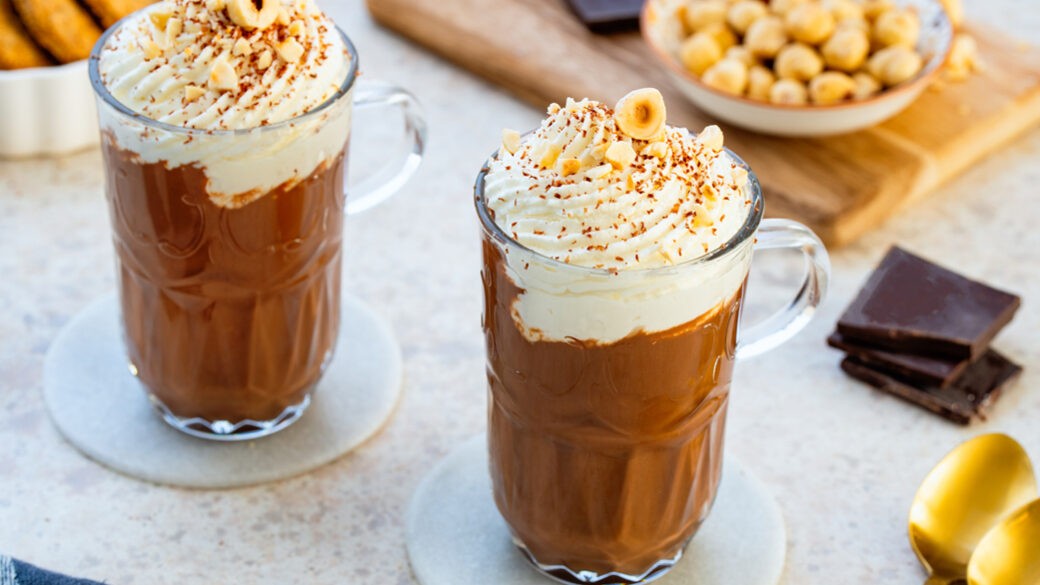 Rich hazelnut hot chocolate with whipped nutty cream and chopped hazelnuts, close-up, warm lighting